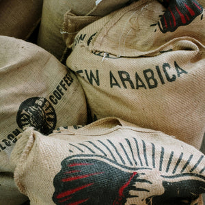Burlap sacks of specialty coffee labeled New Arabica from Garage Coffee Bros. showcasing premium coffee sourcing.